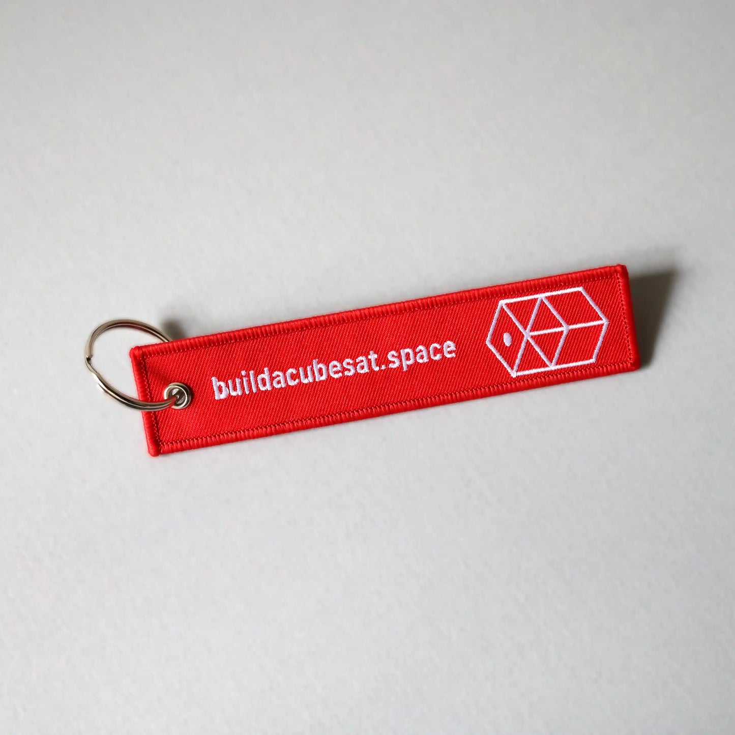 Red keychain with white text and logo on the front side on a light gray background, tilted to the left