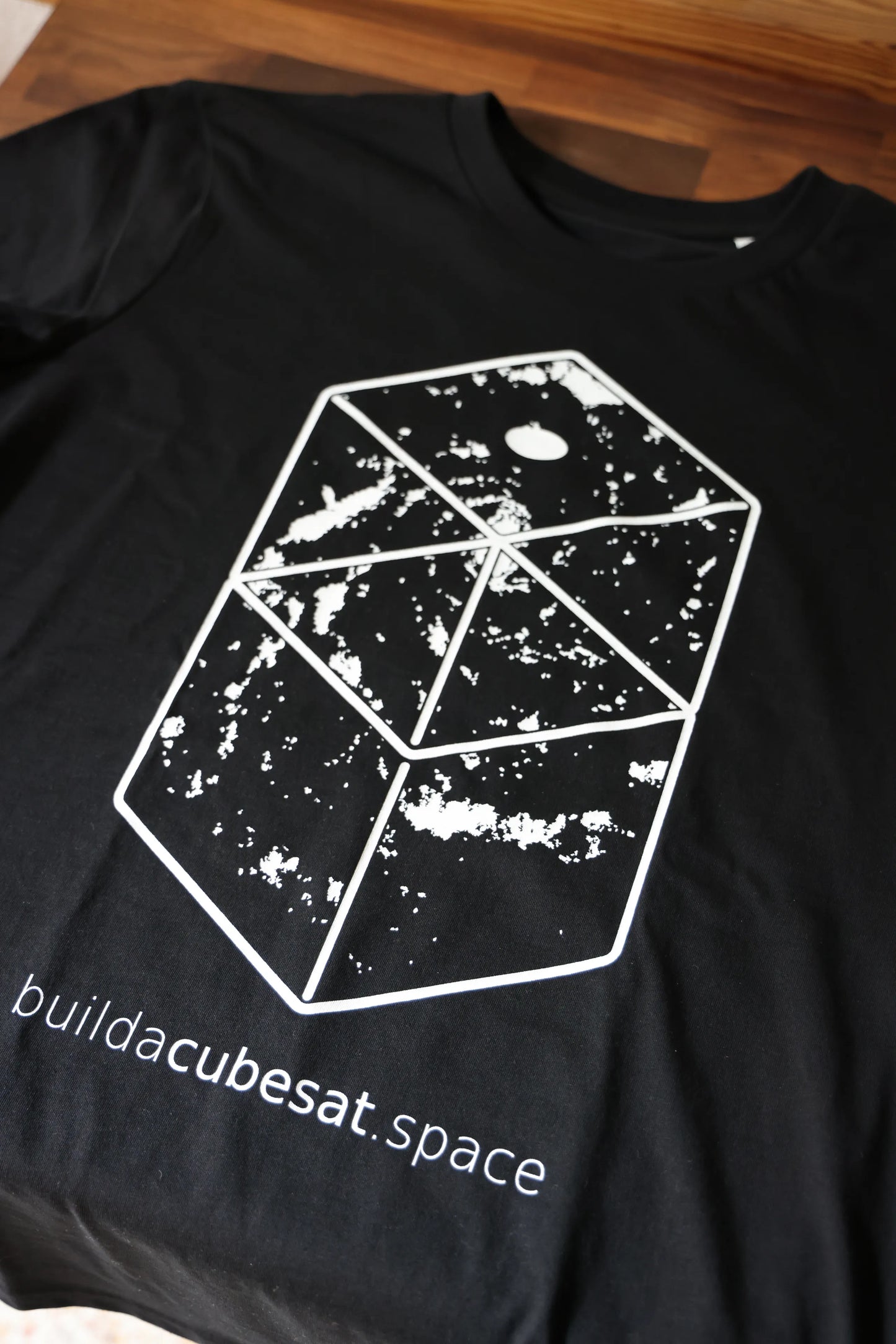 Black t-shirt with a white geometric galaxy design and text on a wooden surface