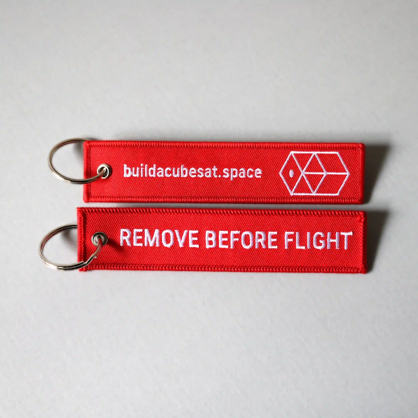 Two red keychains with white text on a gray background, showing the front and back sides of the product