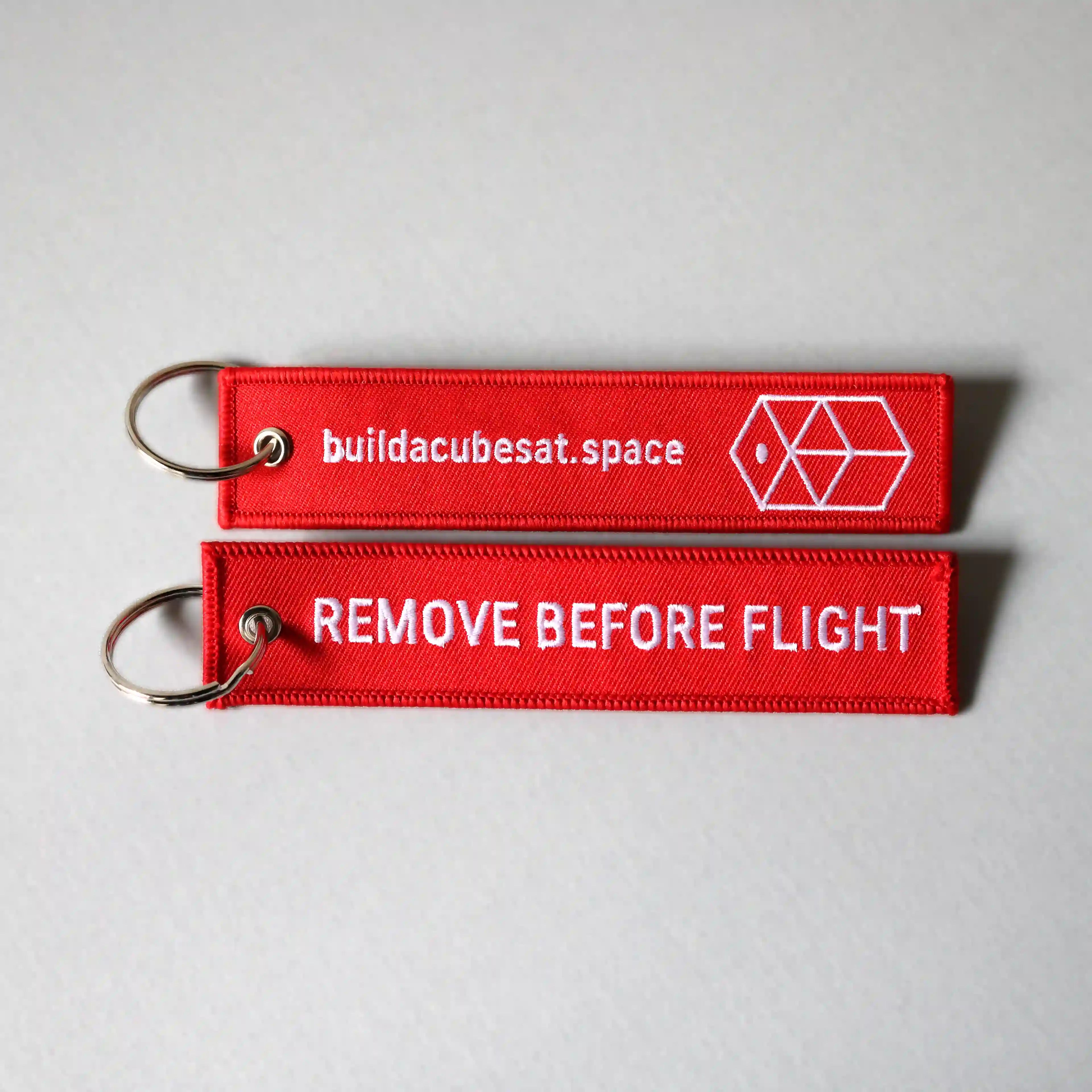 Two red keychains with white text on a gray background, showing the front and back sides of the product