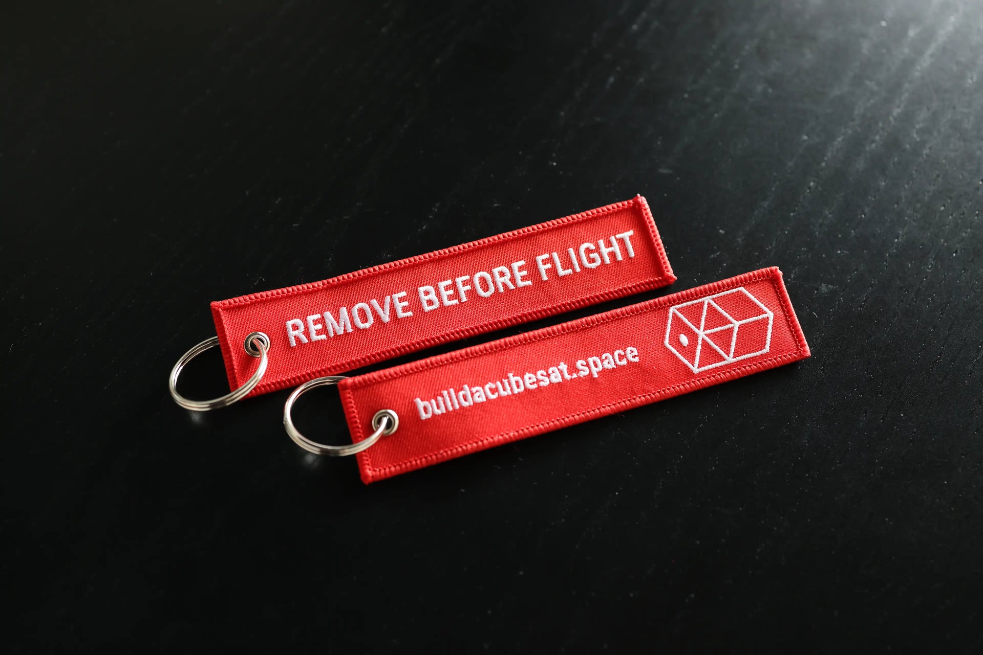 Two red 'Remove Before Flight' tags with a logo on a black background