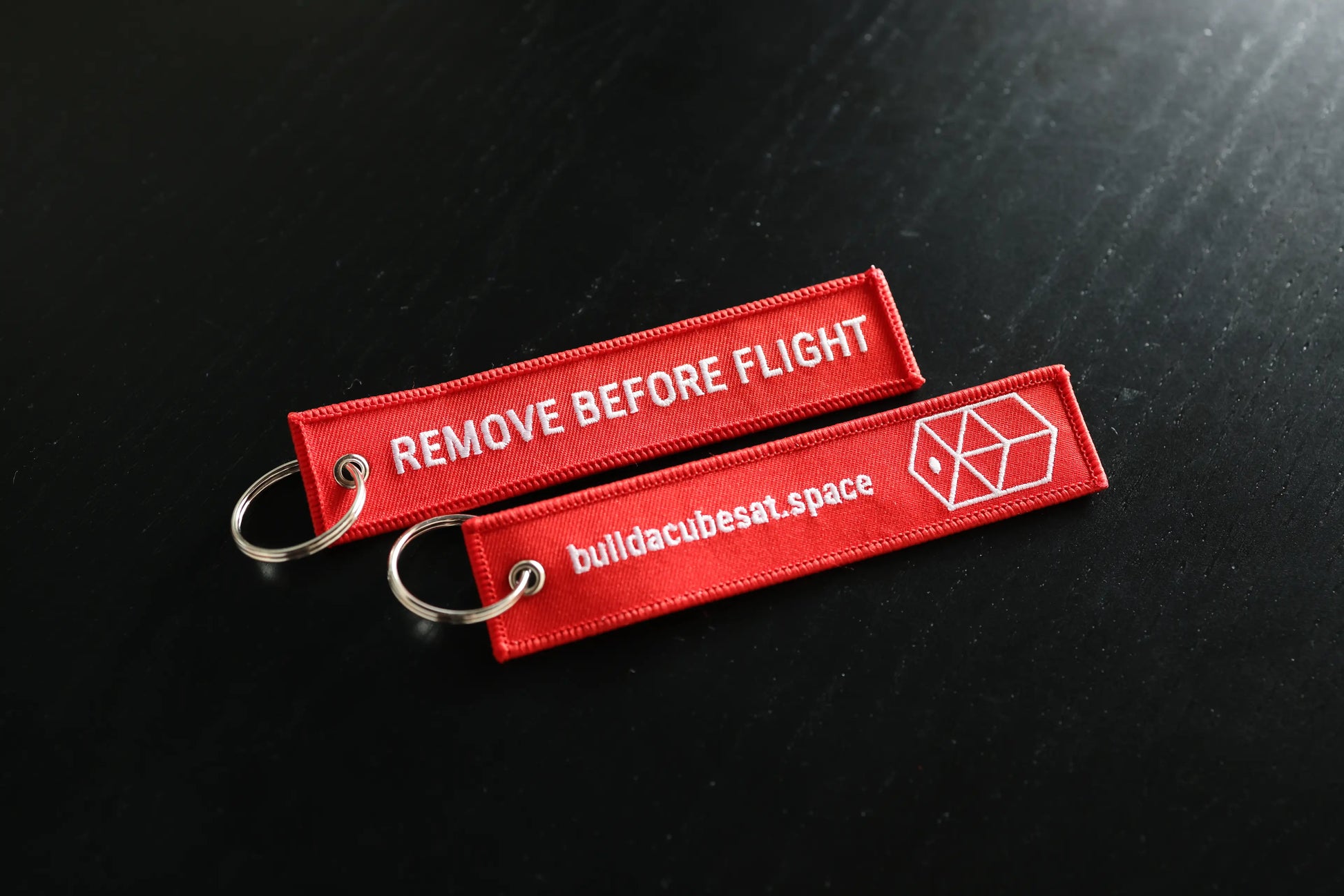 Two red 'Remove Before Flight' tags with a logo on a black background
