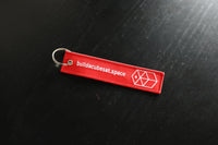 Red keychain with 'buildacubesat.space' text and logo on a black surface