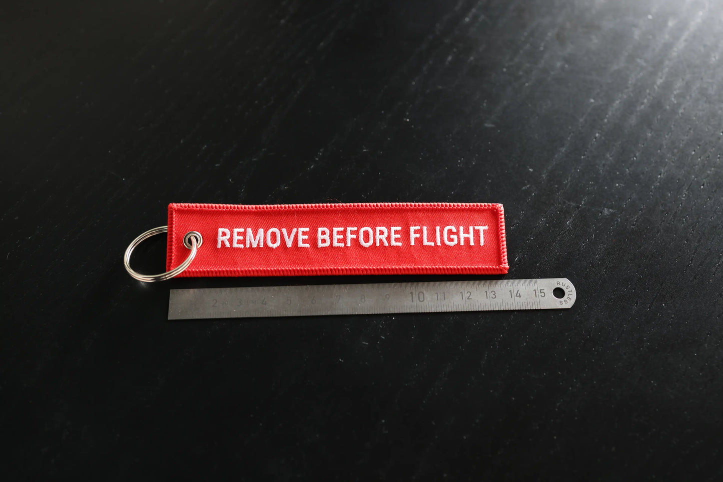 Red 'REMOVE BEFORE FLIGHT' tag on a black background with a ruler for scale.