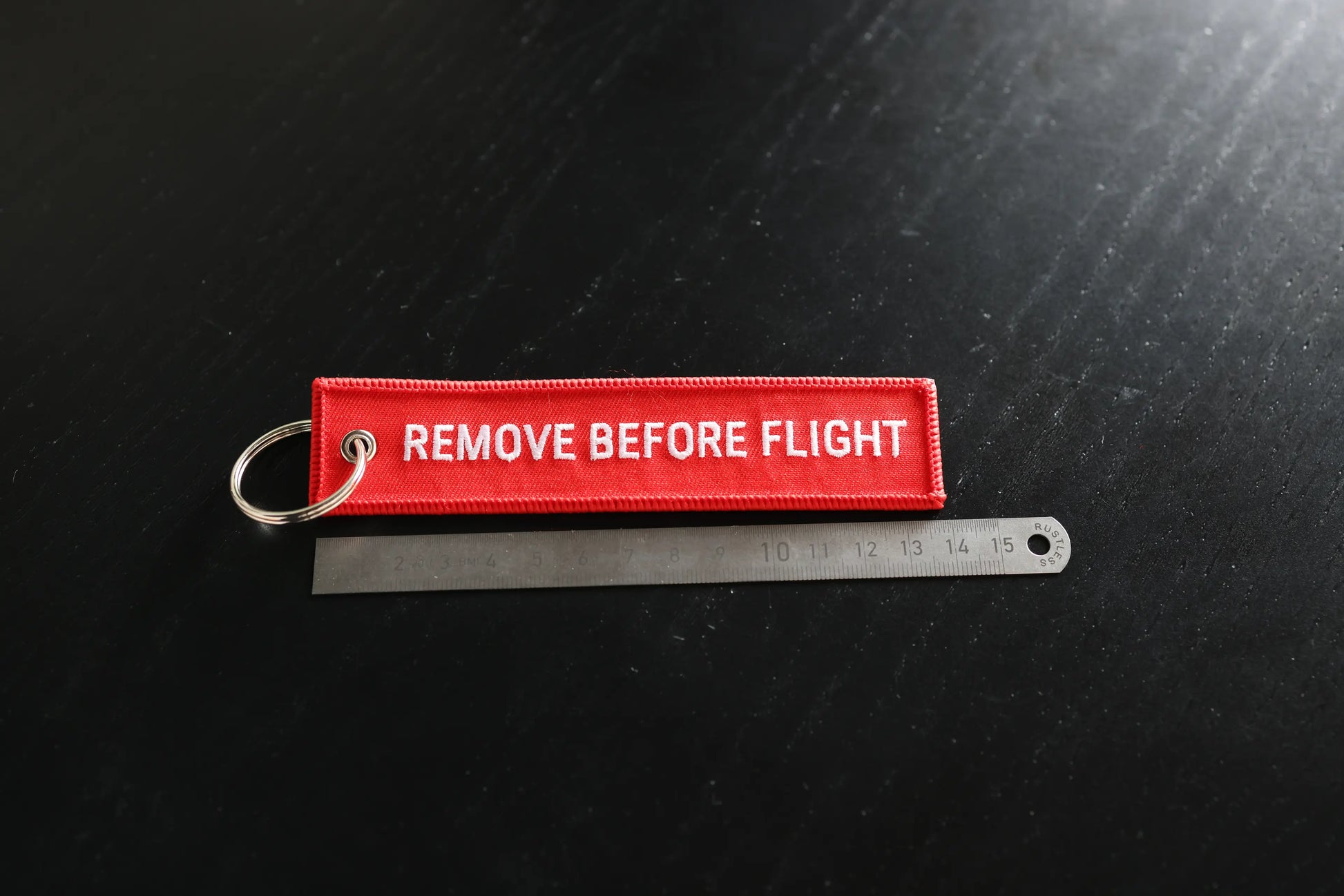 Red 'REMOVE BEFORE FLIGHT' tag on a black background with a ruler for scale.