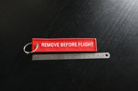 Red 'REMOVE BEFORE FLIGHT' tag on a black background with a ruler for scale.