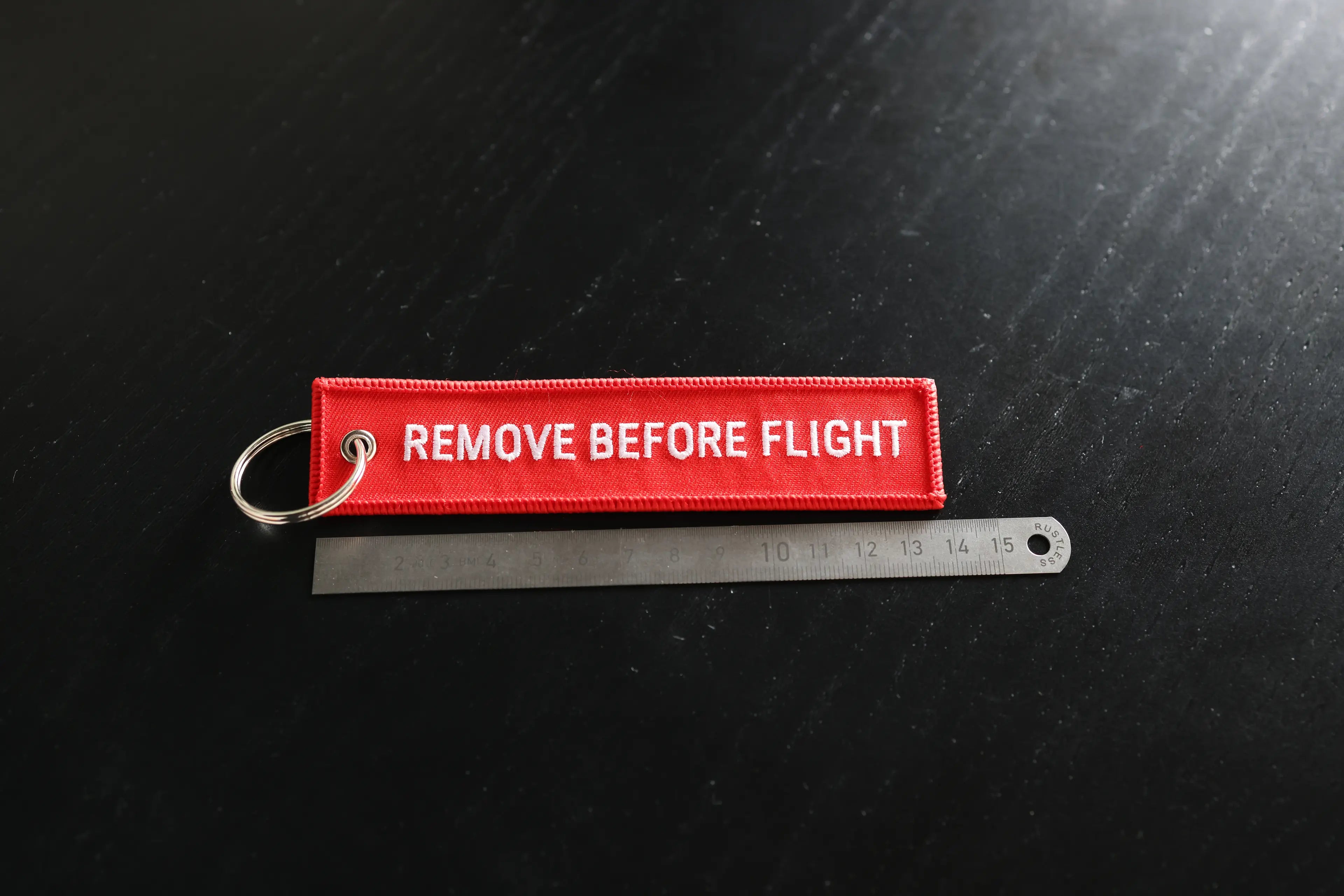 Red 'REMOVE BEFORE FLIGHT' tag on a black background with a ruler for scale.